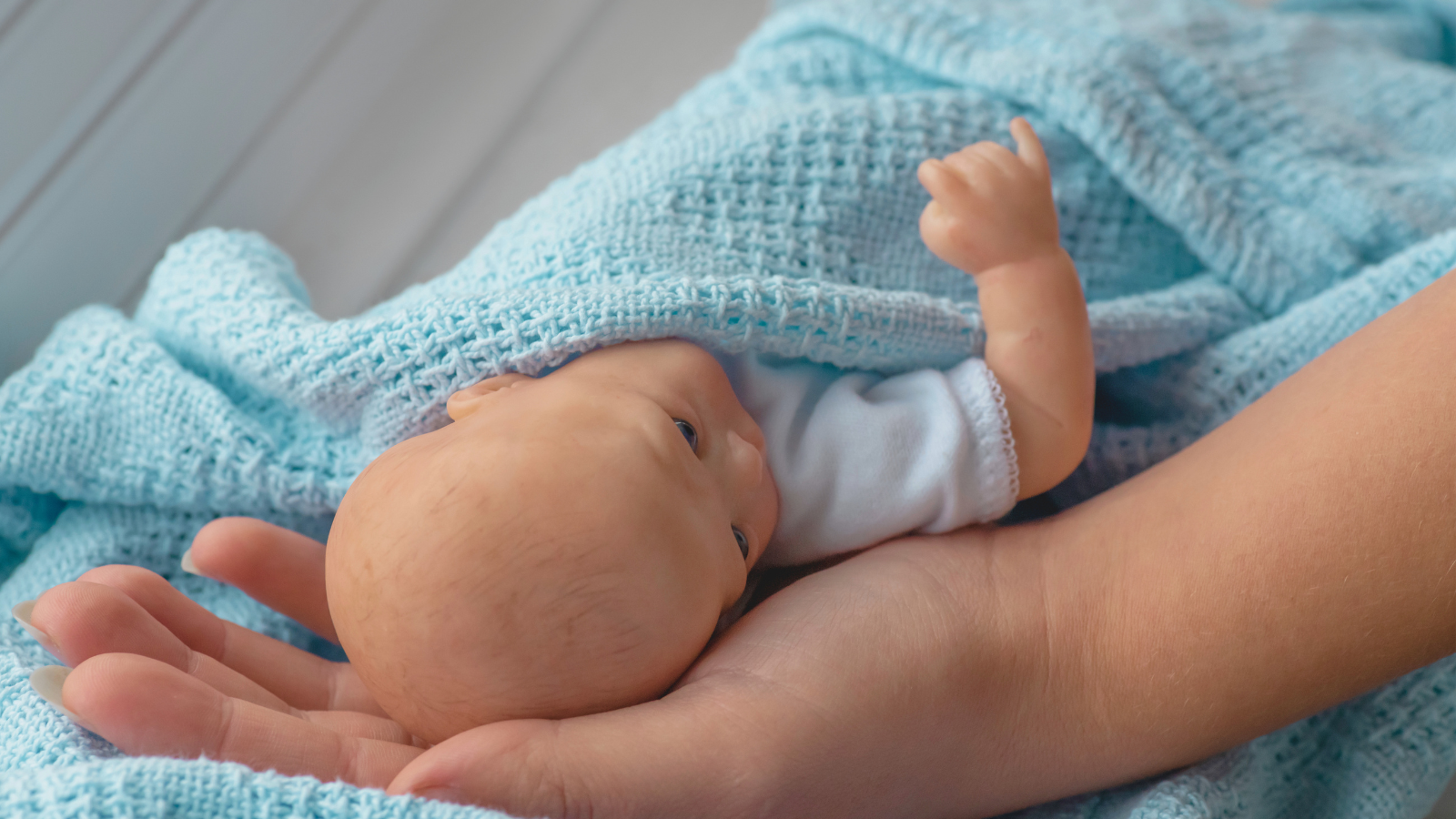 Close-up of hands gently holding a realistic weighted silicone baby doll wrapped in a soft blue blanket