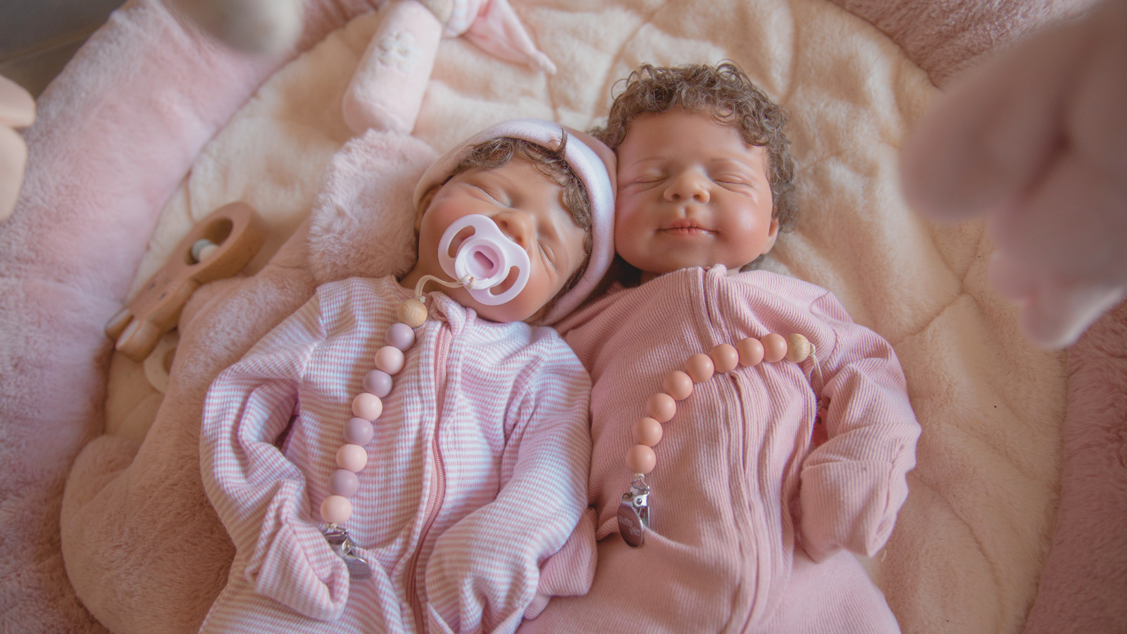 Two realistic weighted silicone baby dolls lying side by side in soft pink outfits, showing calming tactile detail and lifelike design