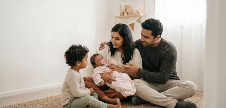 Toddler sitting with parents and a realistic baby doll, representing a new sibling introduction through gentle role play