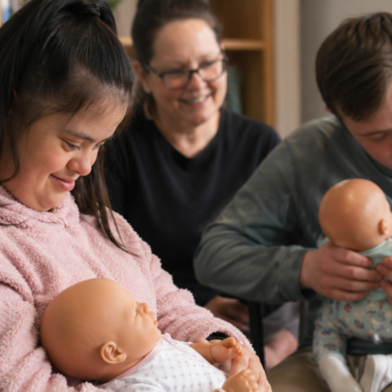 Young adults in a supported setting gently interacting with realistic silicone baby dolls during a guided NDIS support session.