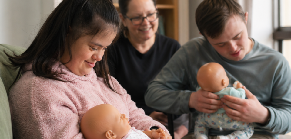 Young adults in a supported setting gently interacting with realistic silicone baby dolls during a guided NDIS support session.
