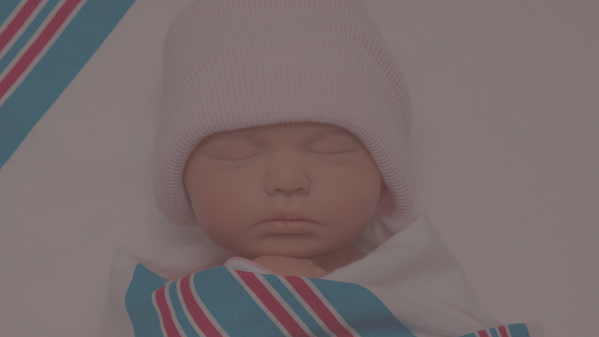 Close-up of a realistic full body silicone Nurtura Baby wrapped in a hospital-style blanket.